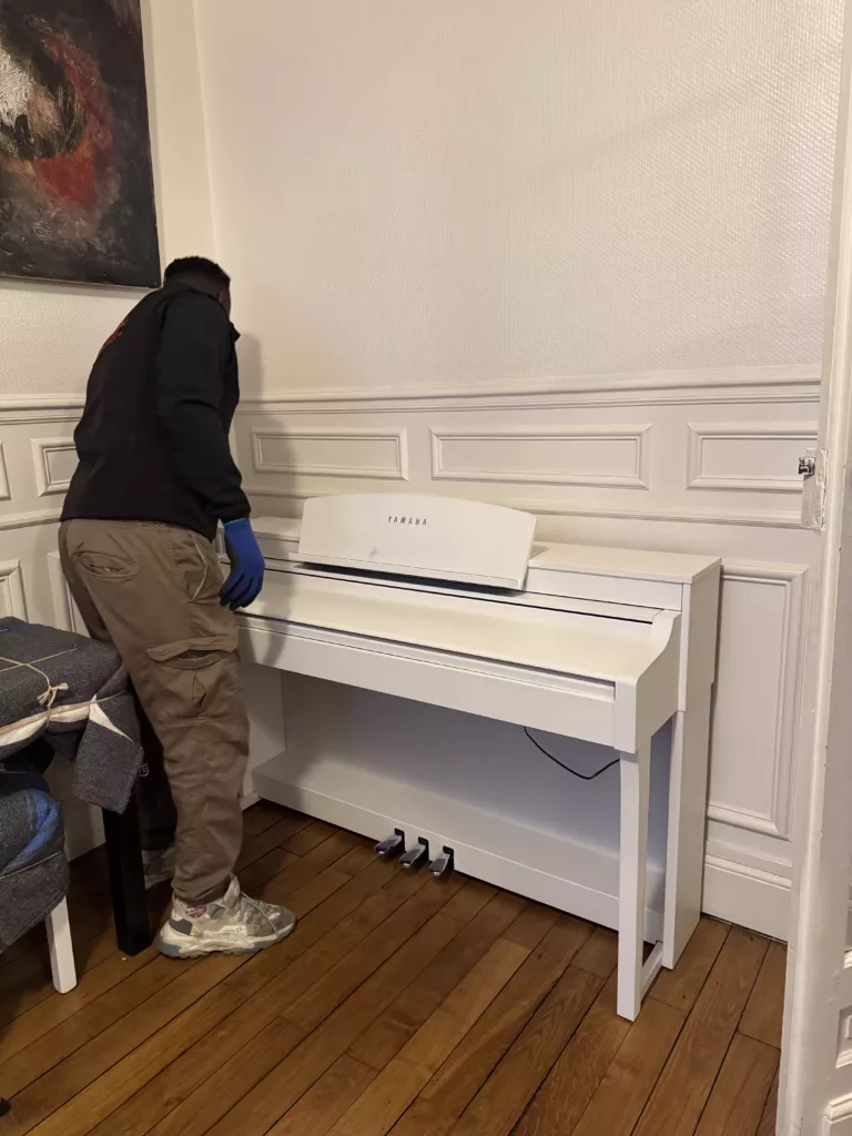 Spécialistes emballant un piano droit avec protections rembourrées avant déménagement